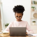 Online Education. African American Girl At Laptop Learning Using Educational Website Sitting At Desk At Home.